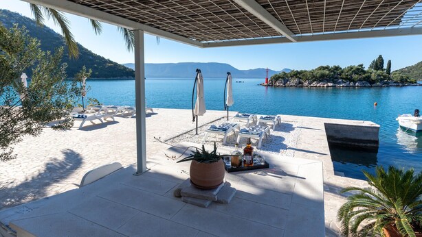 Un salon de plage doté de chaises longues et de parasols, d’une piscine et offrant une vue sur la mer et les collines.