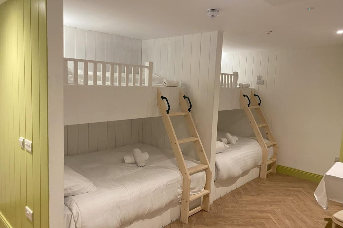 A room with bunk beds, wooden ladders, and a green wall.