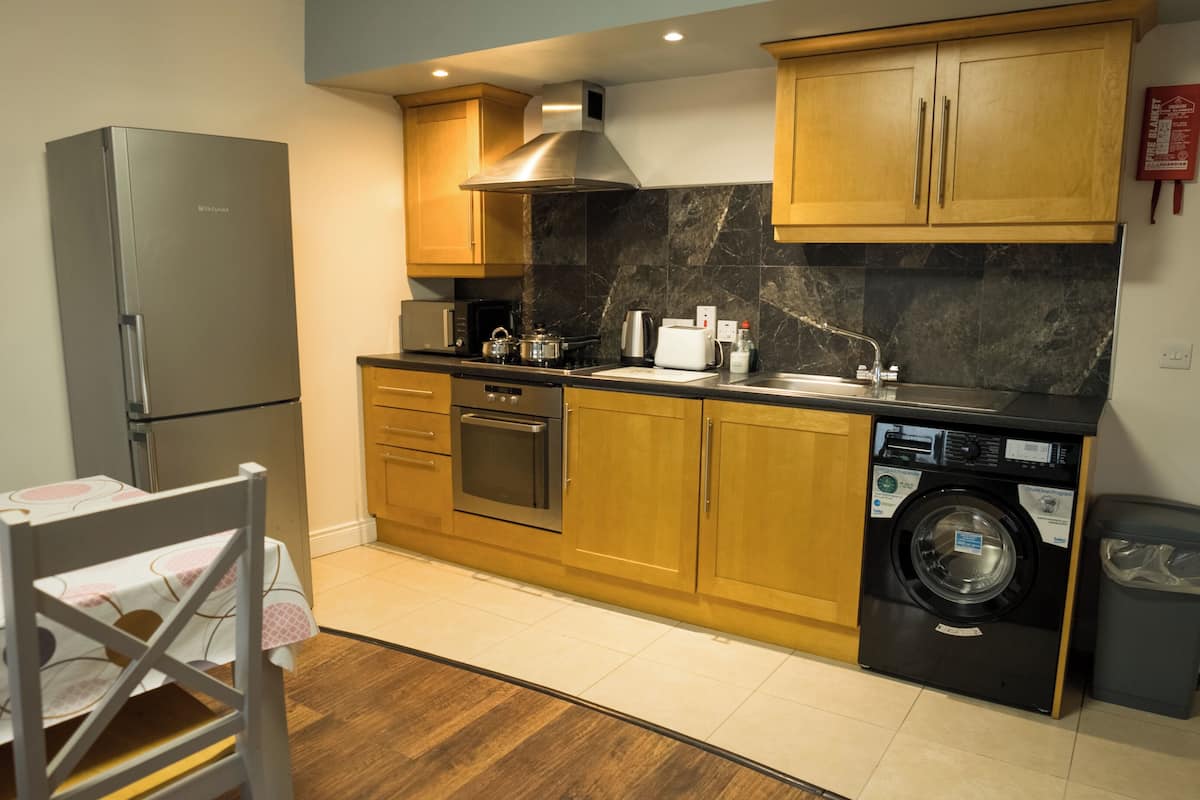 A compact kitchen with wooden cabinets, a stainless steel refrigerator, an oven, a microwave, a toaster, and a washing machine.