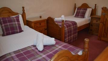 A room with two wooden beds, each with a plaid bedspread and pillows. There are wooden nightstands with drawers and a wooden cabinet.