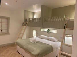 Quarto com beliches, uma escada, uma janela com uma planta e uma cama com manta verde.