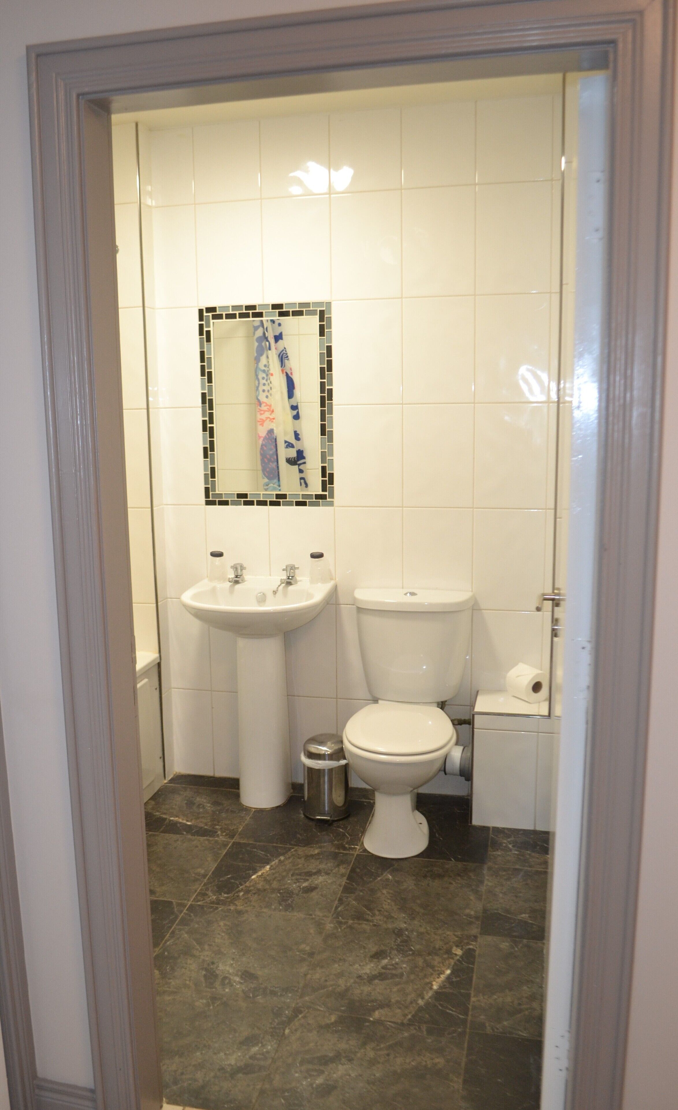 Un baño con lavamanos blanco, inodoro y un pequeño cubo de basura.