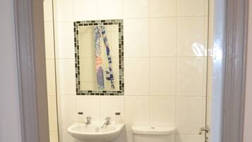 Un baño con lavamanos blanco, inodoro y un pequeño cubo de basura.
