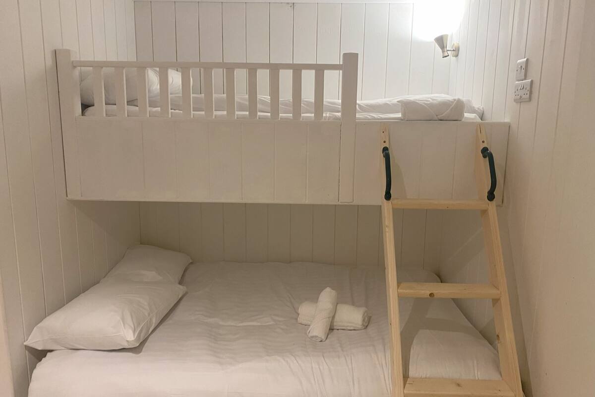 A bunk bed with a ladder, white bedding, and a wall-mounted light fixture.