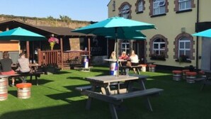 An outdoor patio area with picnic tables and umbrellas, surrounded by a building with arched windows.