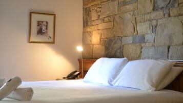 Una habitación de hotel con pared de piedra, una cama con sábanas blancas, un cuadro enmarcado en la pared y un teléfono en la mesita de noche.
