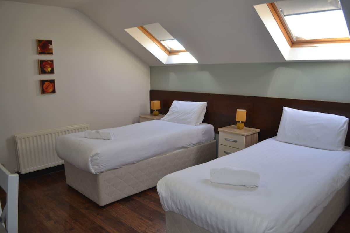 A hotel room with two beds, a skylight, a radiator, and a small table with a lamp.