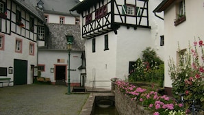 A traditional European courtyard with cobblestone pavement, a narrow water channel, and buildings with exposed timber framing and white walls. - Gästehaus Fries (Blankenheim)