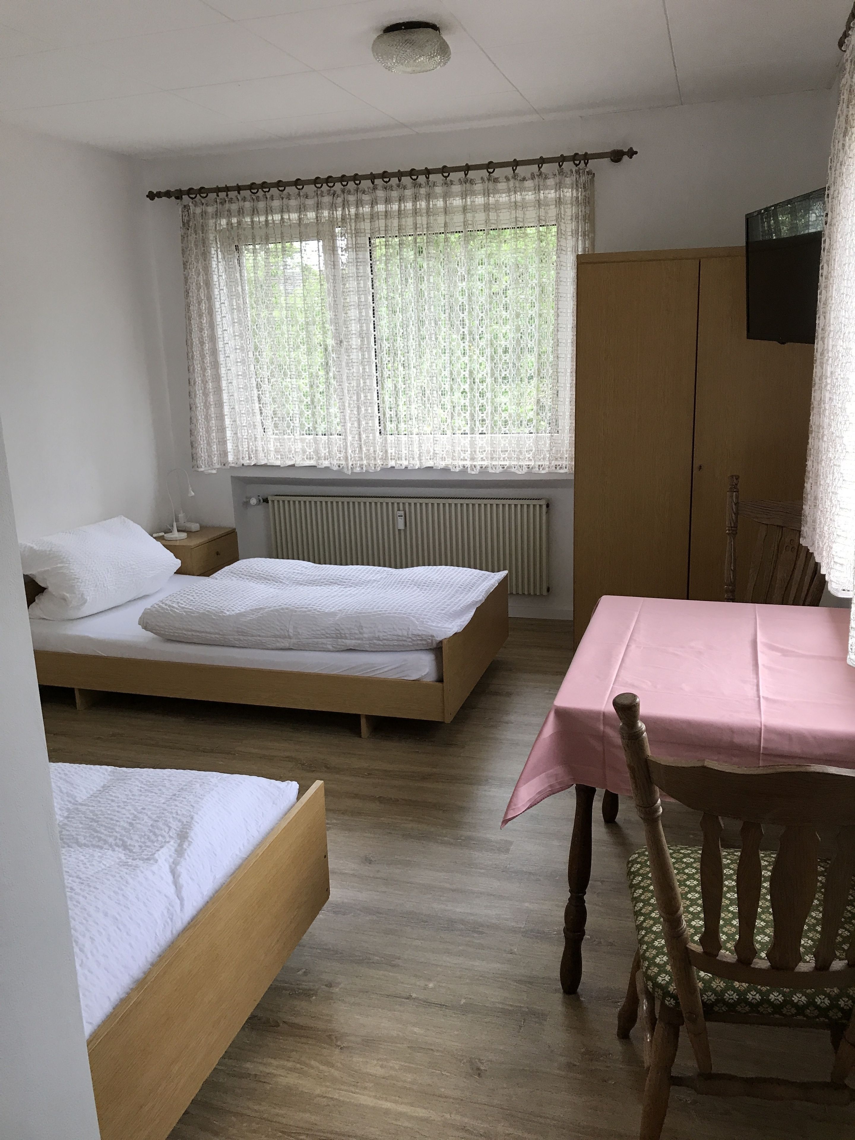 A room with two wooden beds, a table with a pink tablecloth, and a chair with a floral tablecloth.