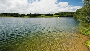 A clear lake with a boat and buoys, surrounded by green hills and trees. - Gästehaus Fries (Blankenheim)