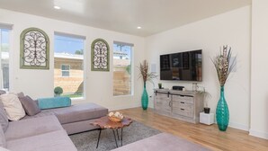 Ein modernes Wohnzimmer mit einem grauen Sofa, einem Holztisch, einem Fernseher und dekorativen Vasen.