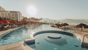 A pool area with lounge chairs and umbrellas, a hot tub, and a view of mountains and a city skyline. - 17th-Floor Beachfront Grand Venetian Condo ☆Panoramic Bay Views & Infinity Pools (Puerto Vallarta)