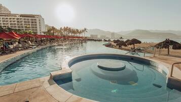 Un espace piscine avec des chaises longues et des parasols, un jacuzzi, et une vue sur les montagnes et le panorama urbain.
