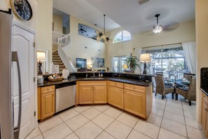 A kitchen with a curved island, wooden cabinets, and a dining area with wicker chairs. - Heated Pool | Gulf Access Canal | Dock | BBQ (Cape Coral)