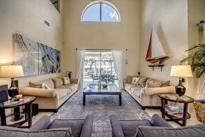 A spacious living room with a high ceiling, two sofas, a coffee table, and a sailboat decoration. - Heated Pool | Gulf Access Canal | Dock | BBQ (Cape Coral)