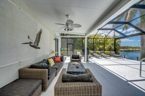 Un patio iluminado por el sol con mobiliario de mimbre, un ventilador de techo y vistas a un cuerpo de agua.