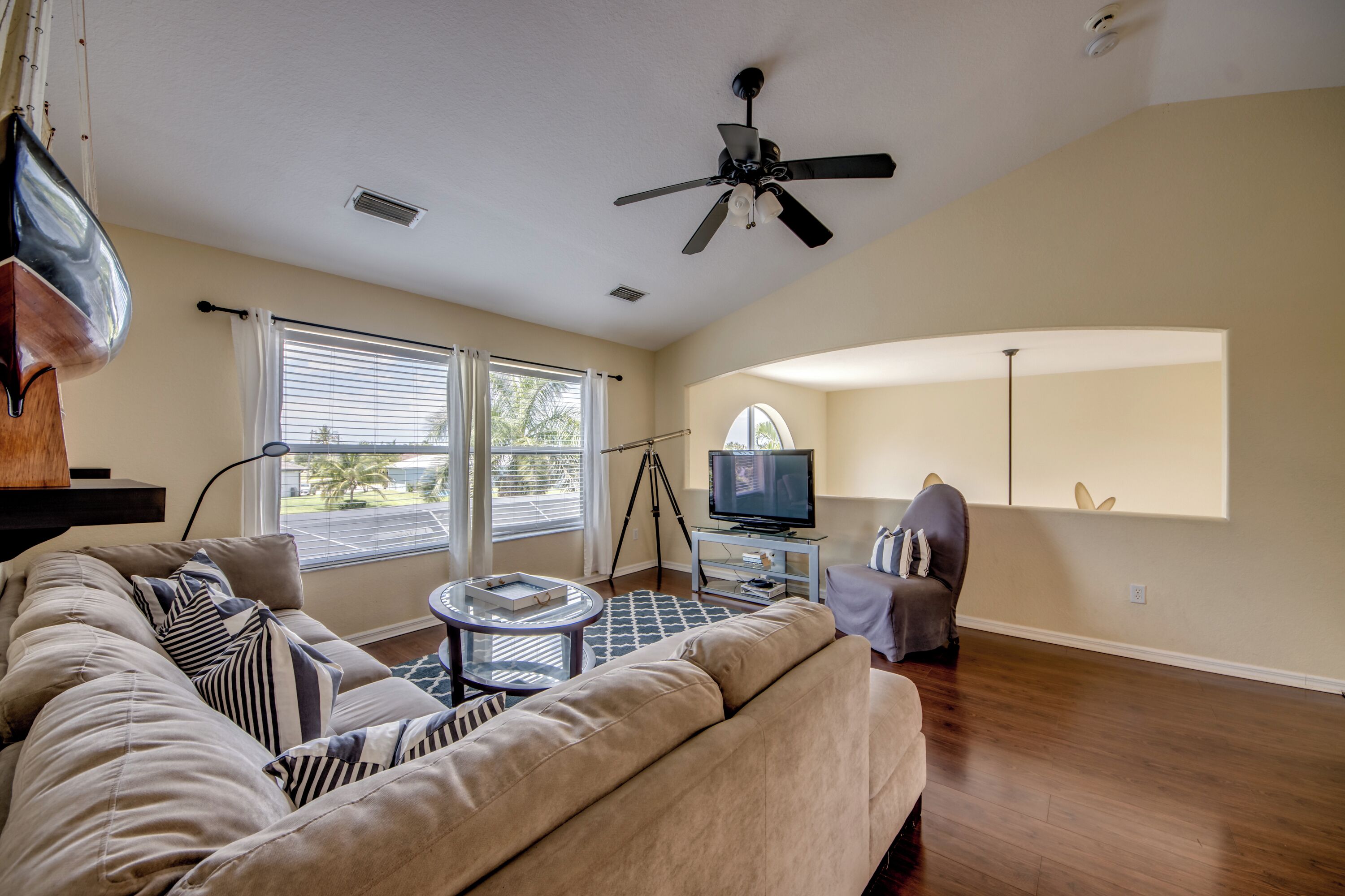 A living room with a sofa, a television, a ceiling fan, and a window with blinds.