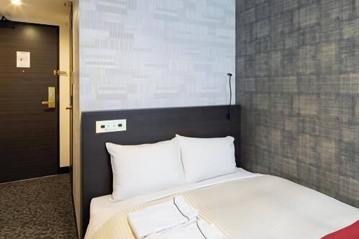 A hotel room with a bed, a dark headboard, a red accent wall, and a patterned carpet.