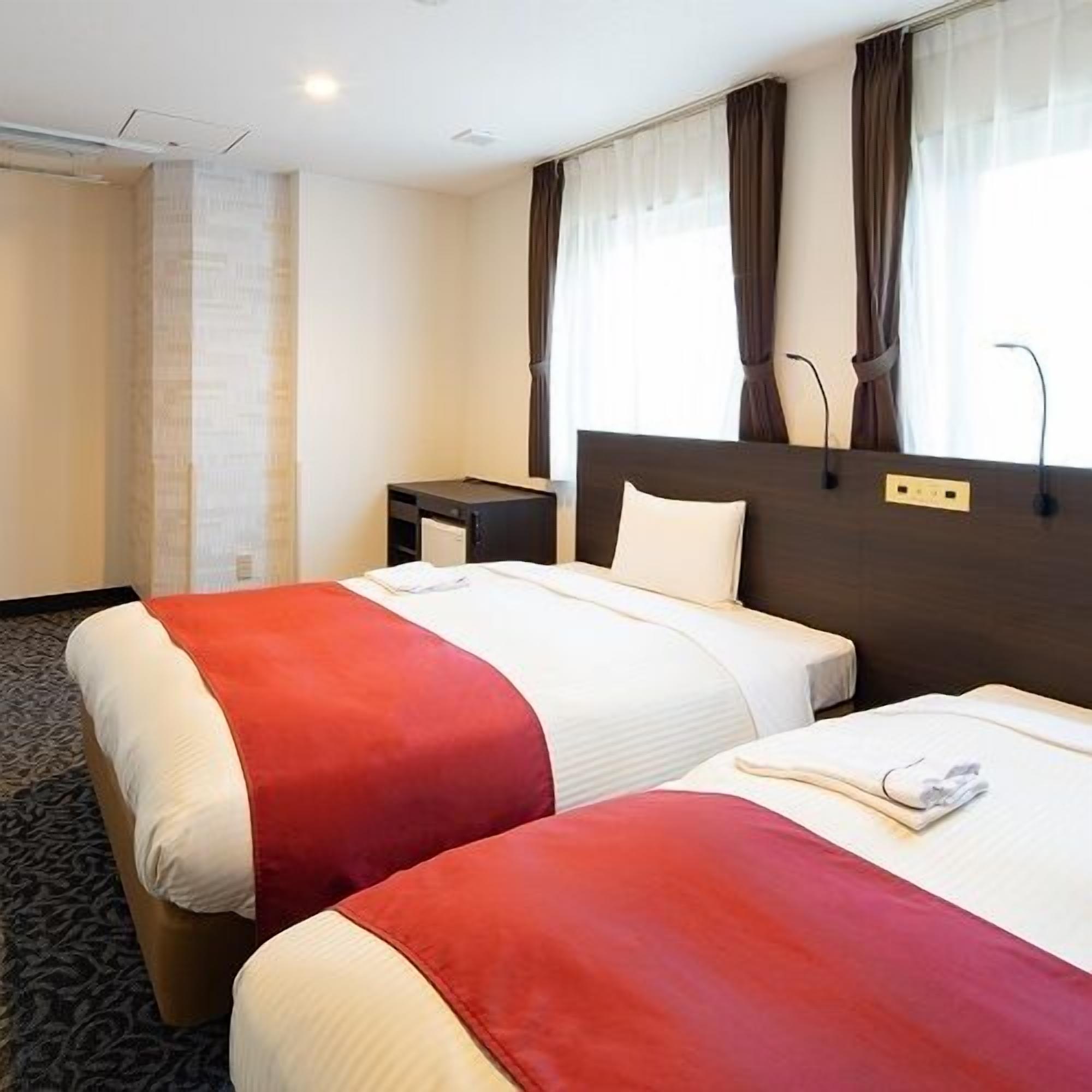 A hotel room with two beds, a nightstand, and a window with curtains.