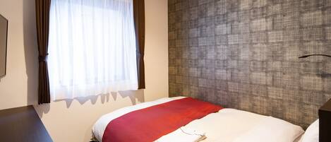 A hotel room with a bed, a window with curtains, a textured wall, and a desk.