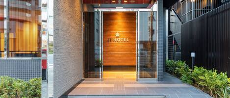 A modern hotel entrance with a glass door, a sign reading "HOTEL", and a tiled pathway leading to the entrance.