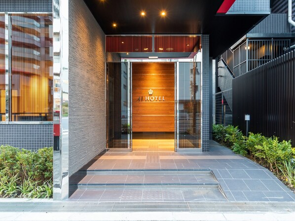 A modern hotel entrance with a glass door, a sign reading "HOTEL", and a tiled pathway leading to the entrance.