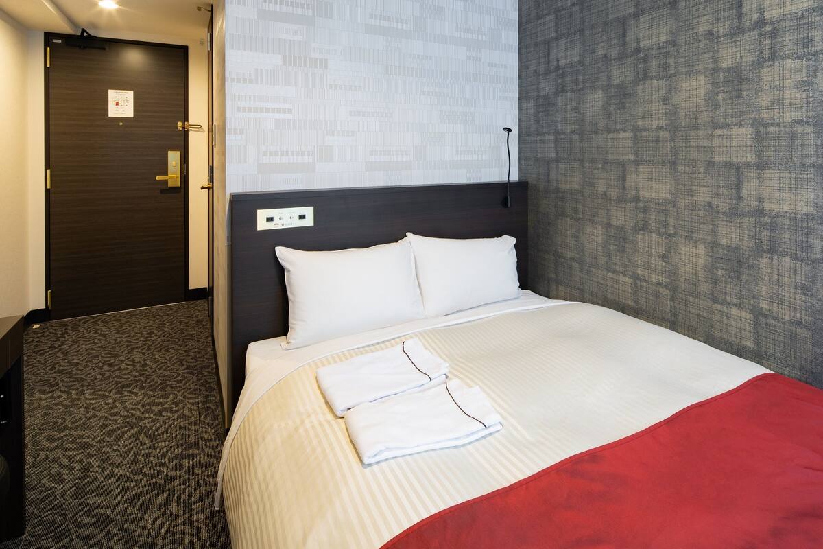 A hotel room with a bed, a headboard, a wall with a patterned design, and a door.