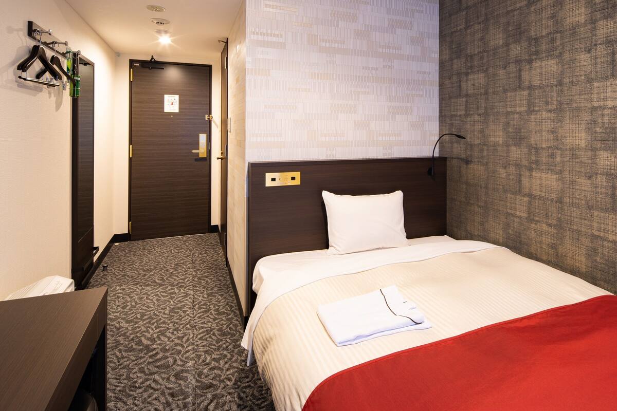 A hotel room with a bed, a desk, and a wardrobe.
