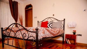 A bedroom with a wooden floor, a metal bed frame, a patterned bedspread, and a red rug. - Sherry Homes Qwetu Studio (Nairobi)