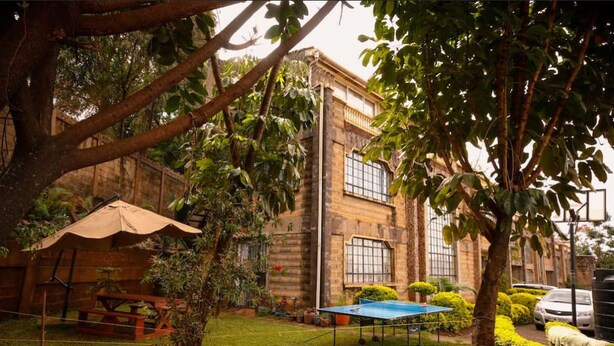A building with a brick facade, a tennis court, and a picnic table in a well-maintained garden. - Sherry Homes Qwetu Studio (Nairobi)