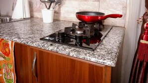 A kitchen with a gas stove, a red frying pan, and a set of kitchen utensils in a white container. - Sherry Homes Qwetu Studio (Nairobi)