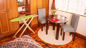 A compact room with wooden cabinets, a small table with chairs, a mirror, and a window with curtains. - Sherry Homes Qwetu Studio (Nairobi)