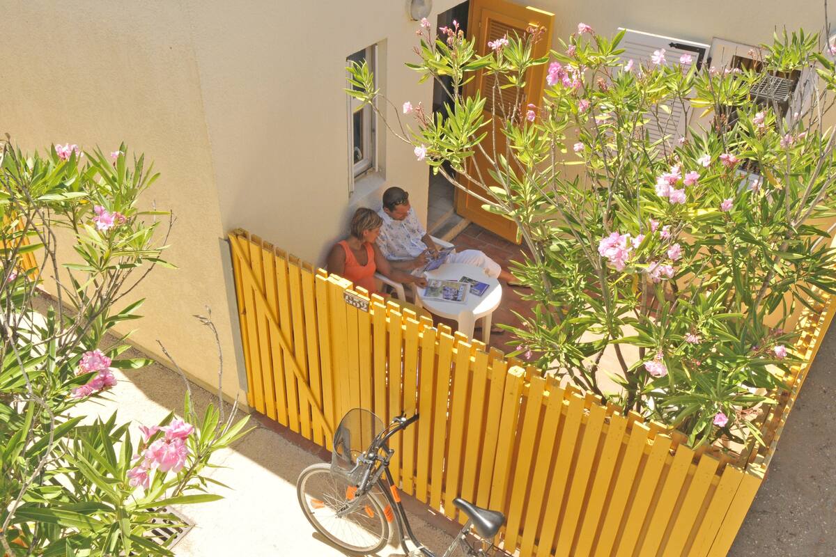 A courtyard with a yellow fence, a bicycle, and flowering plants.