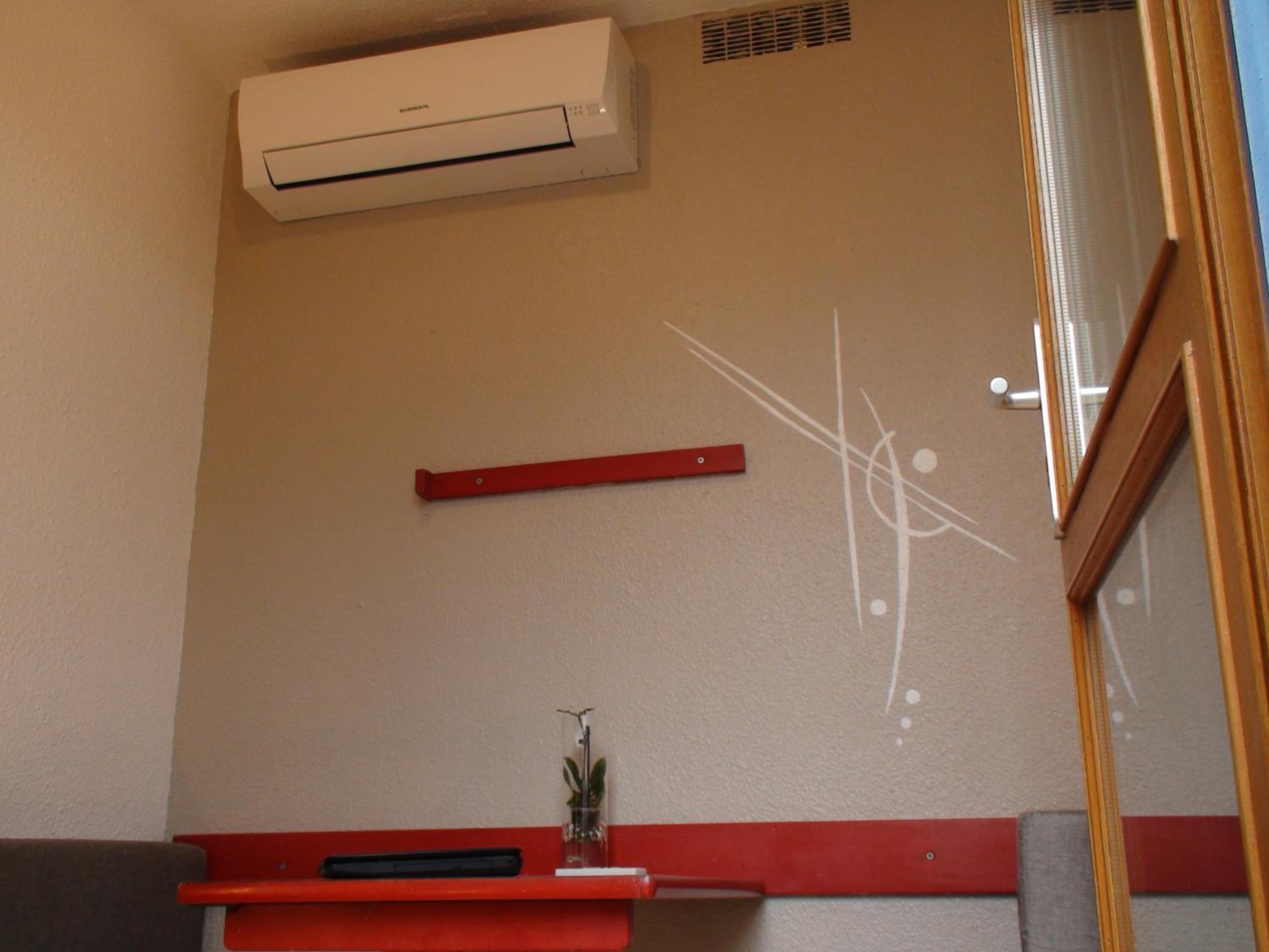 Una habitación con un aire acondicionado blanco, un estante rojo y una planta pequeña.