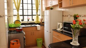 A kitchen with wooden cabinets, a stove, a refrigerator, a microwave, and a vase with flowers on the counter. - Sherry Homes Raha Westlands (Nairobi)