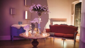 A round wooden table with glassware and flowers, a red sofa, and a purple wall with a mirror and a cabinet. - Assteas Bed & Breakfast (Montesarchio)