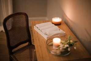 A wooden table with a white tray holding folded towels, a lit candle, and a glass bowl with flowers. - Assteas Bed & Breakfast (Montesarchio)