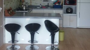 A modern kitchen with three black bar stools, a microwave, and a refrigerator. - Tongyeong Camellia House (Tongyeong)