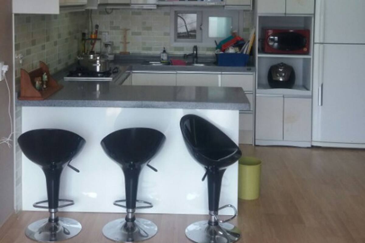 A modern kitchen with three black bar stools, a microwave, and a refrigerator.