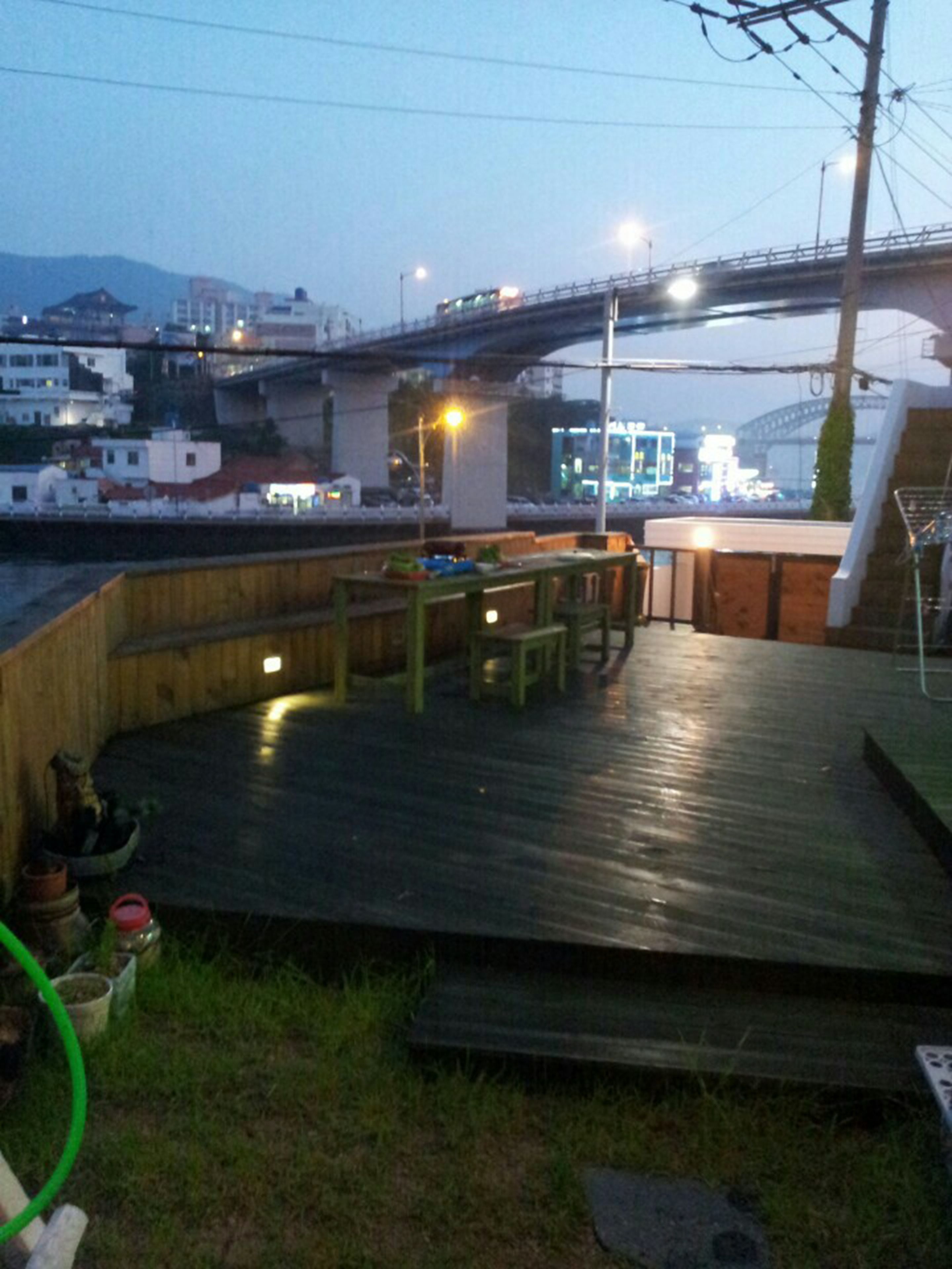An outdoor deck with wooden benches and tables, a green hose, and a view of a bridge and buildings in the background.