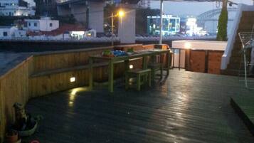 An outdoor deck with wooden benches and tables, a green hose, and a view of a bridge and buildings in the background.