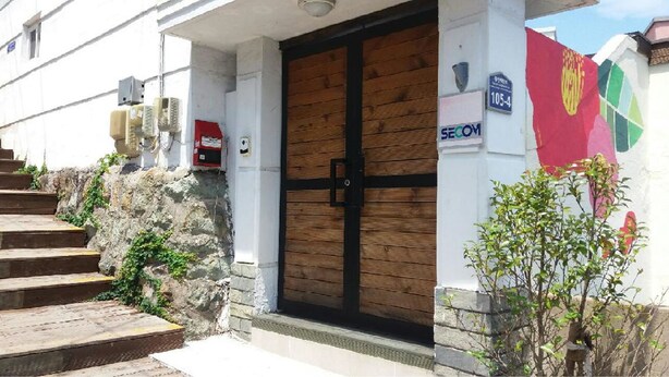 A building entrance with a wooden door, a staircase, and a small garden area. - Tongyeong Camellia House (Tongyeong)