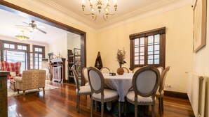 A dining area with a round table, six chairs, and a chandelier. There are wooden floors and a view of a living room with a red chair and a white table. - Yuyuan Impression Guesthouse (Shanghai)