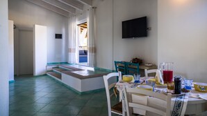 Ein Essbereich mit einem für zwei Personen gedeckten Tisch, einem an der Wand befestigten Fernseher und einer Treppe, die zu einer oberen Ebene führt.