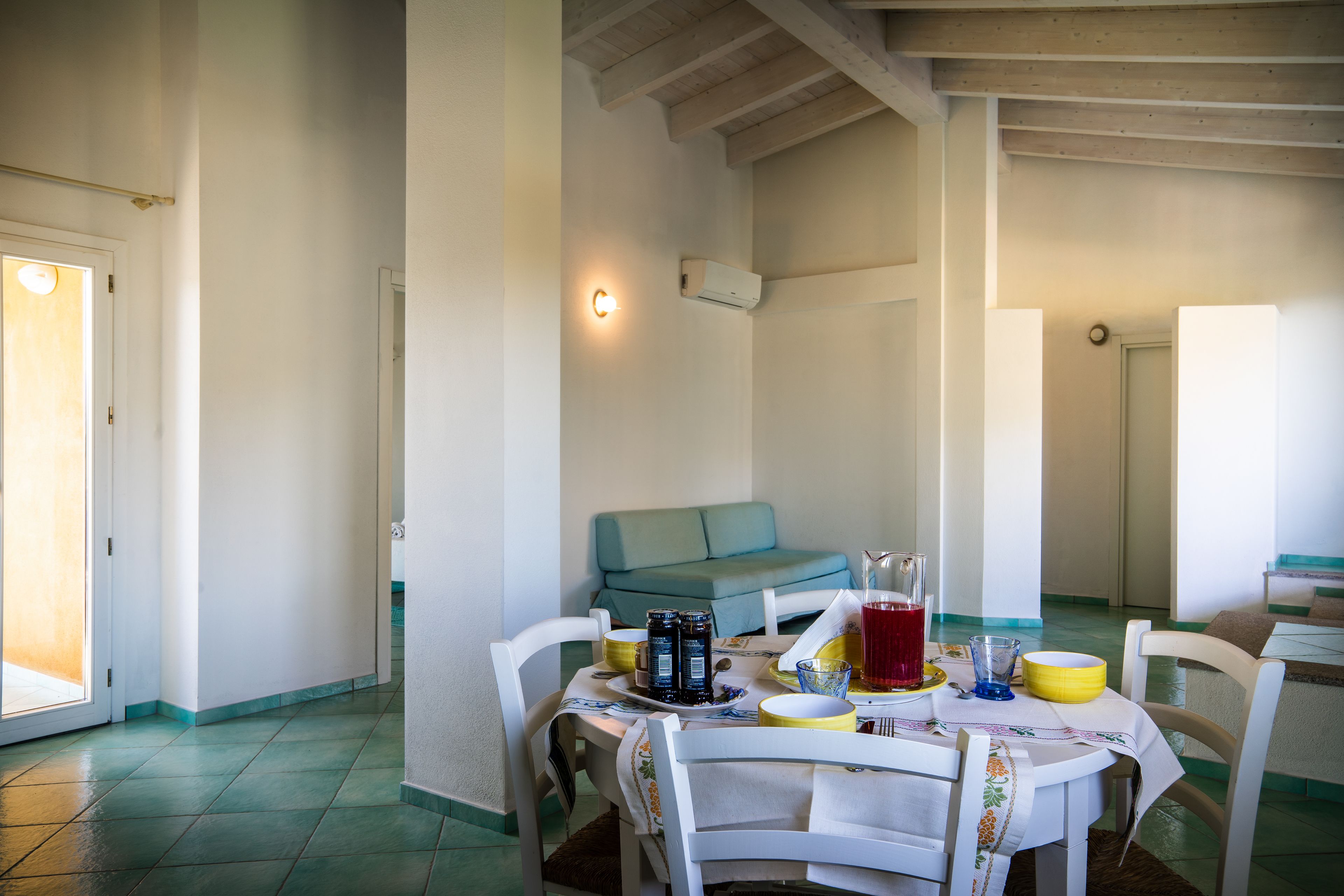 Un coin repas avec une table dressée pour deux personnes, un canapé et un climatiseur fixé au mur.
