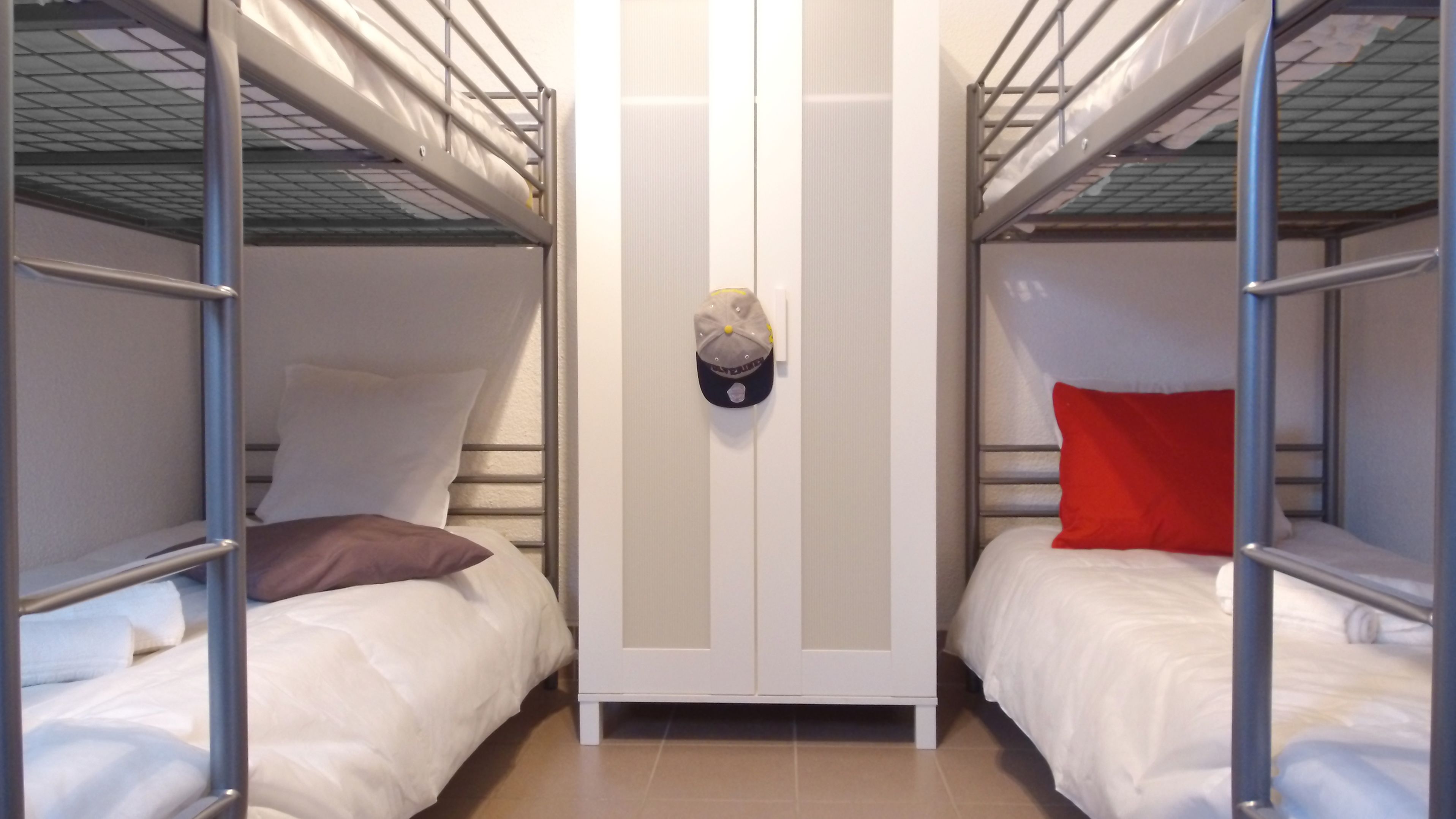A bunk bed room with two beds, a wardrobe, and a hat hanging on the wall.