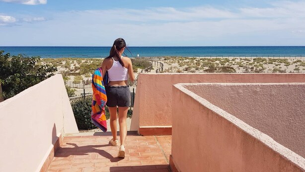 Eine Frau geht auf einem Balkon mit Blick auf Strand und Meer.