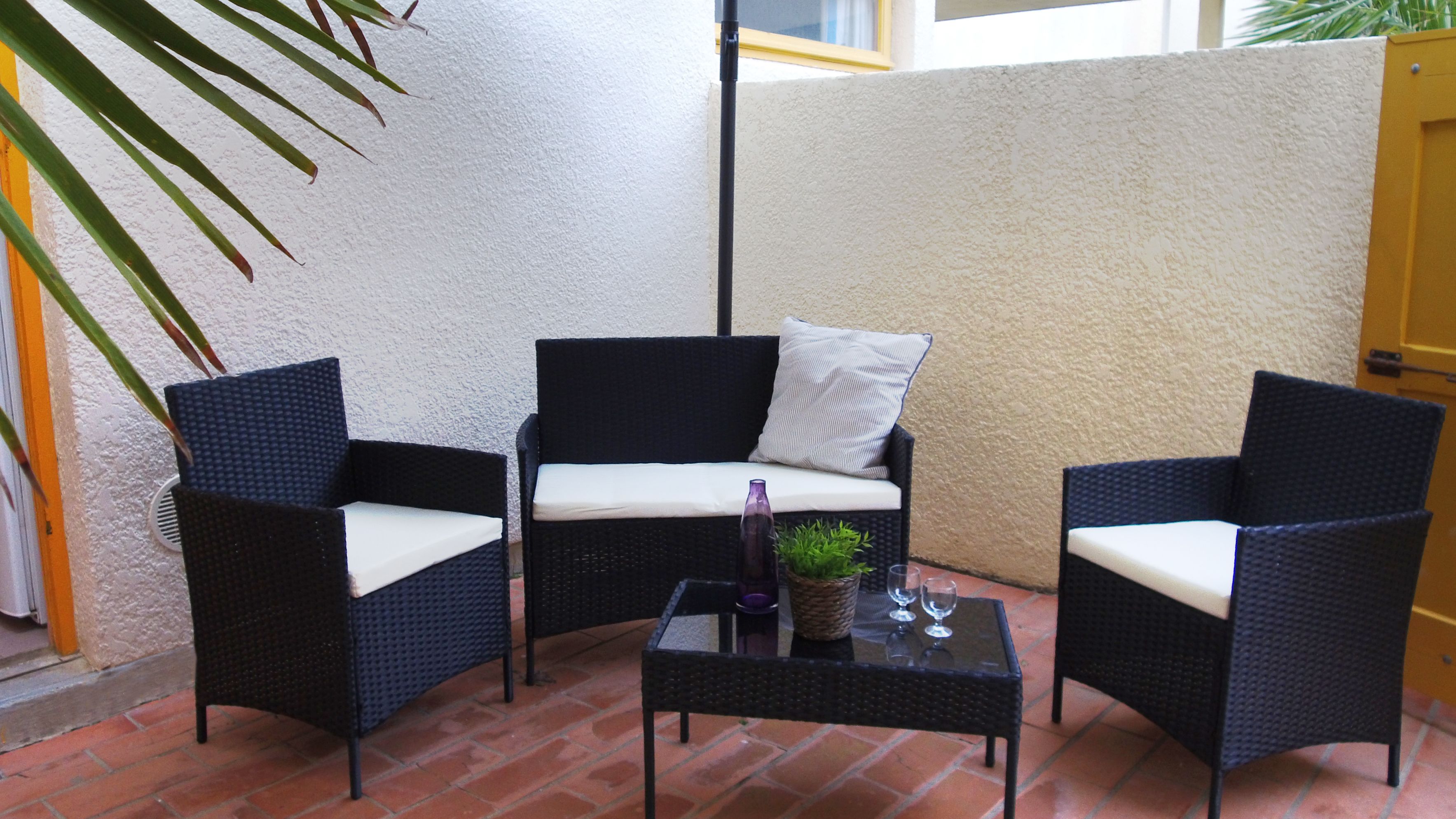 Un patio amueblado con mobiliario de mimbre, incluyendo dos sillones y una mesita, con un cojín en el sofá.