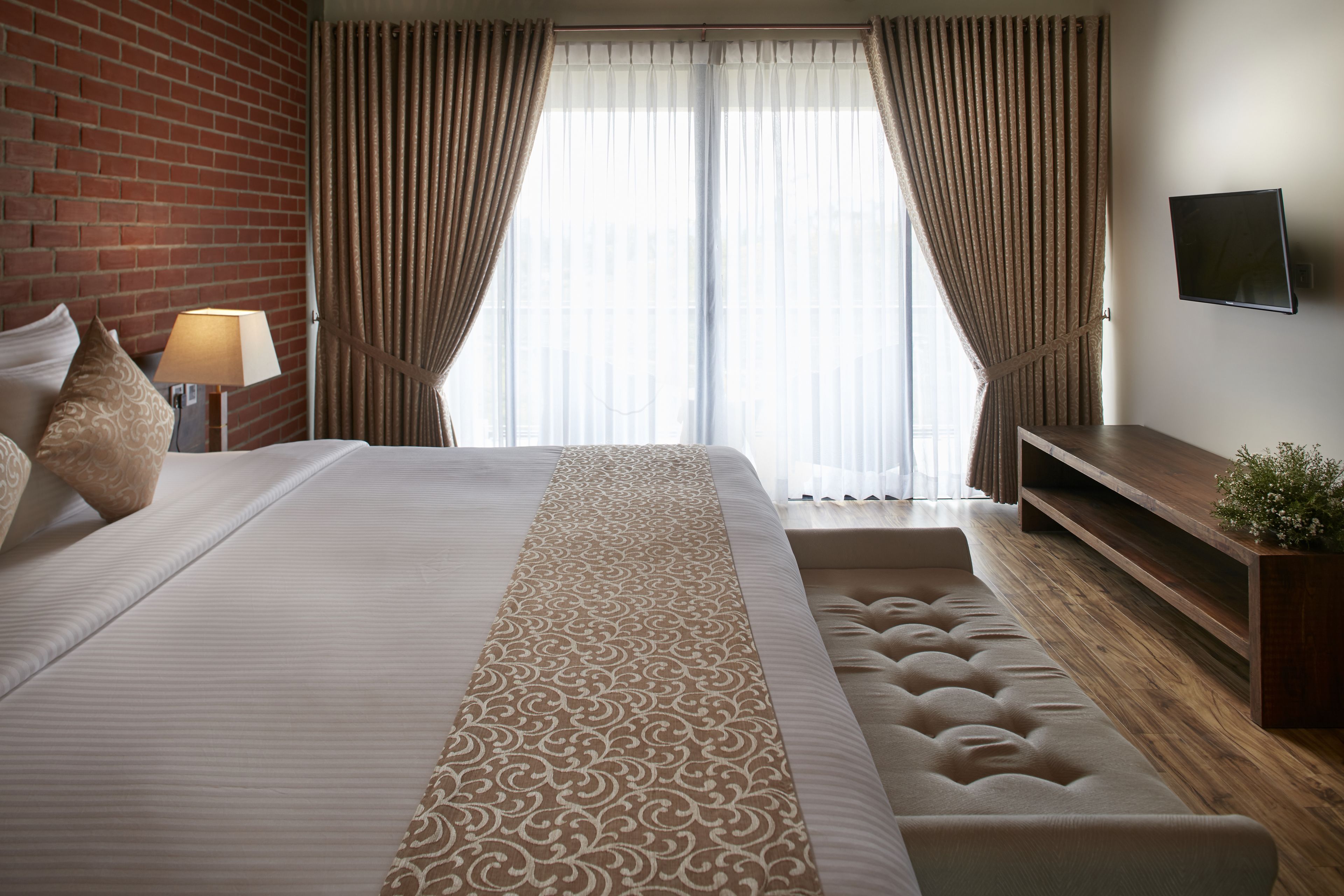 Een hotelkamer met een groot bed, een aan de muur bevestigde televisie en een houten bank.