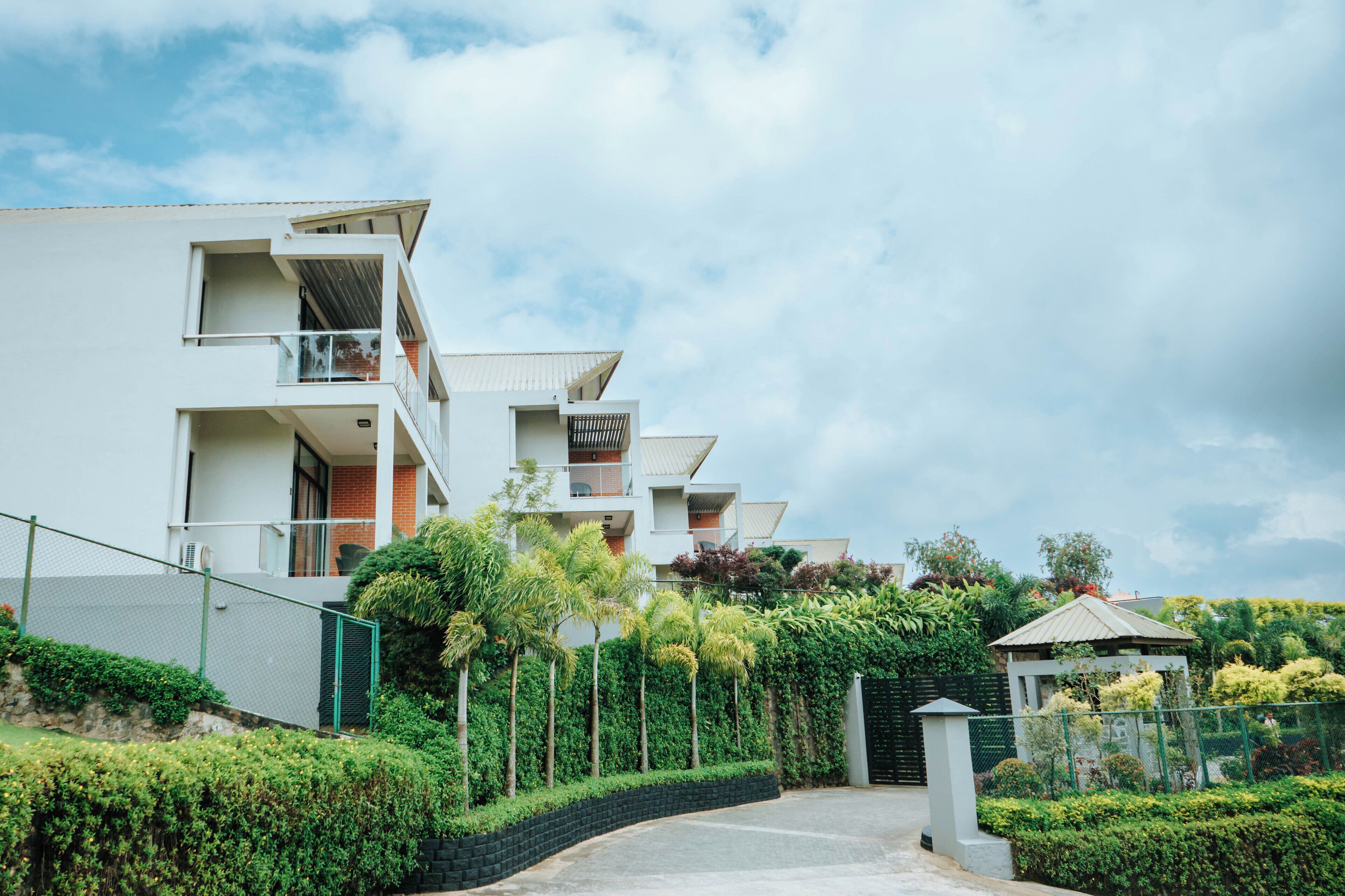 Un edificio residencial moderno con varios balcones, entrada protegida y abundante vegetación.